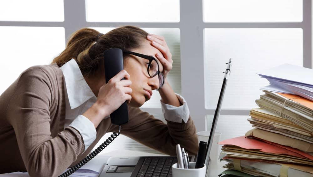 An overwhelmed business owner handling a phone call beside a stack of paperwork